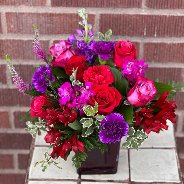 Mixed bouquet of red, pink, and purple flowers in a dark vase