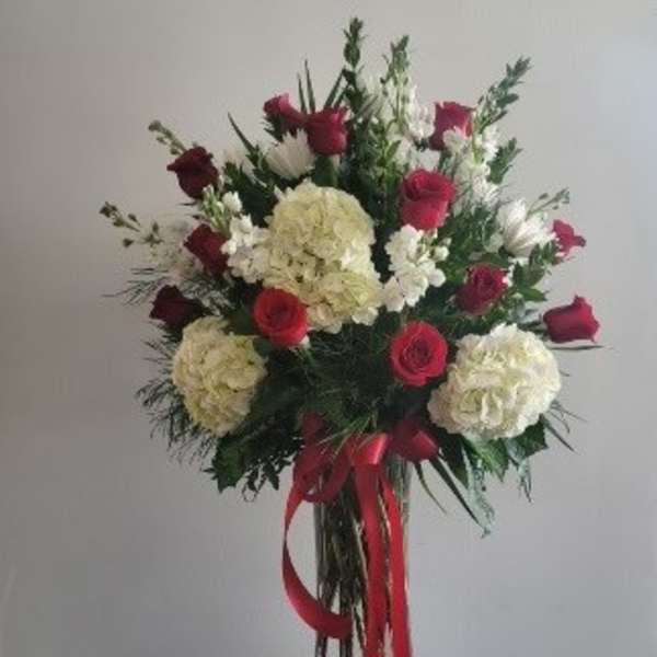 Tall bouquet of red roses and white hydrangeas in a glass vase with red ribbon