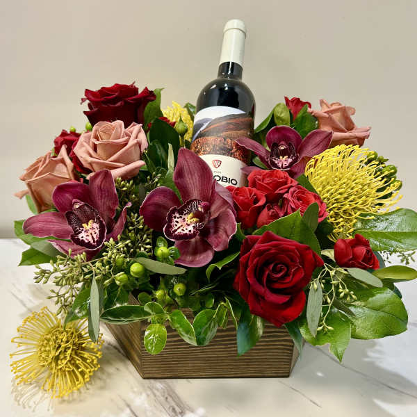 Floral arrangement with roses, orchids, and a wine bottle in a wooden box