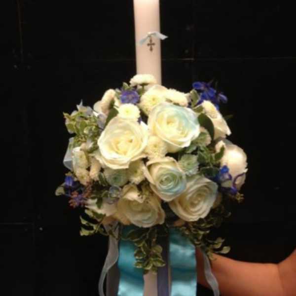 White rose floral arrangement with a tall candle and blue ribbons