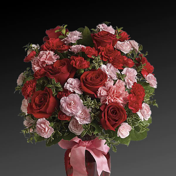 Red roses and pink carnations in a red vase with a pink ribbon