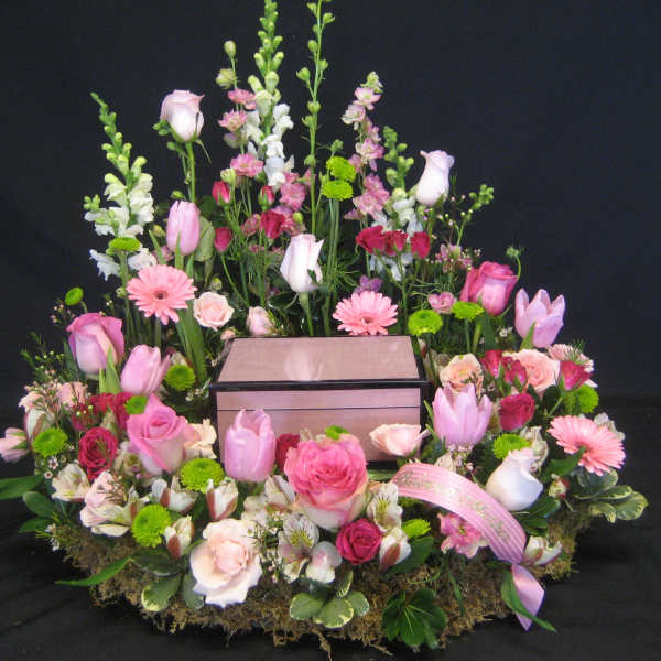Pink and white floral arrangement surrounding a wooden box on a black background