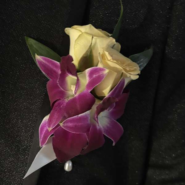 Boutonniere with cream roses and purple orchids on black fabric