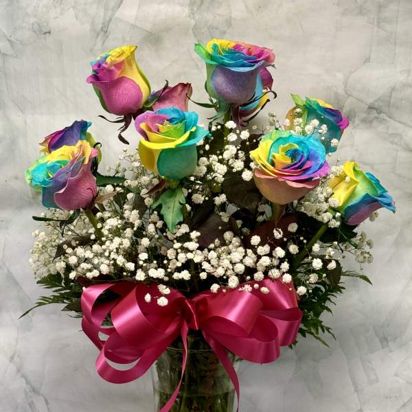 Rainbow-colored roses in a glass vase with a pink ribbon