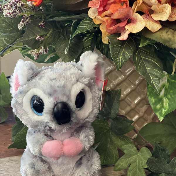 Plush koala toy in front of a floral arrangement with orange blooms