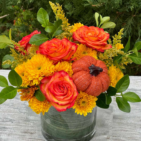 Orange roses and yellow mums in a glass vase with a small pumpkin accent