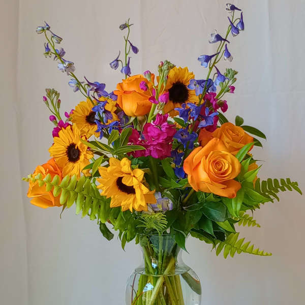 Bouquet of orange roses, sunflowers, and blue flowers in a glass vase