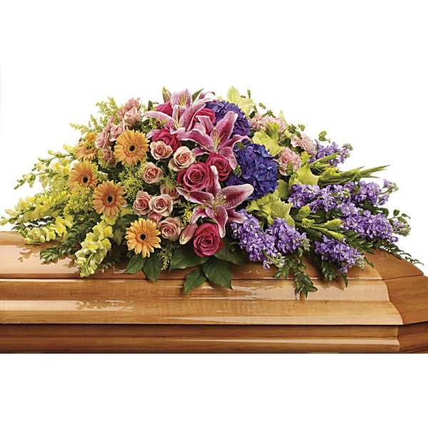 Colorful casket spray of pink lilies, roses, yellow gerbera daisies, and purple flowers on a wooden casket