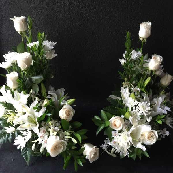 Two white floral sprays with roses and lilies arranged in a heart shape