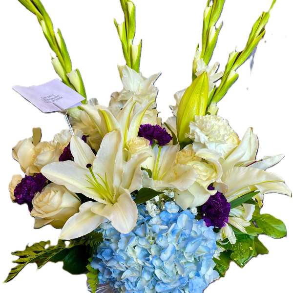White lilies, cream roses, purple carnations, and blue hydrangea in a glass vase
