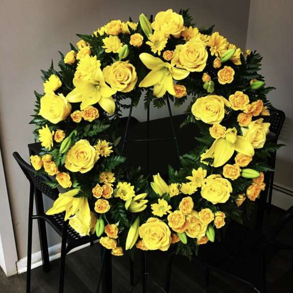 Yellow floral wreath with roses, lilies, and daisies on a stand