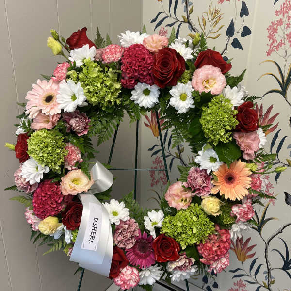 Heart-shaped floral wreath with roses, daisies, and carnations on an easel