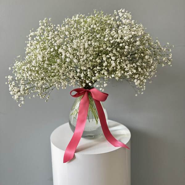White baby's breath bouquet in a glass vase with a pink ribbon