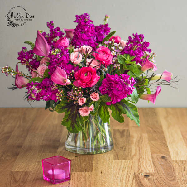 Pink and magenta floral arrangement in a clear glass vase with a pink candle holder nearby