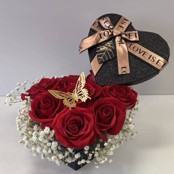 Red roses in a black heart-shaped box with white baby's breath and a ribbon bow