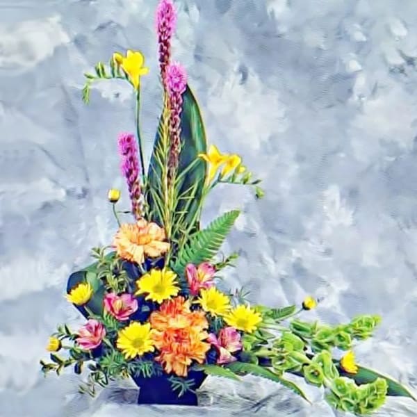 Tall asymmetrical arrangement with yellow, orange, pink, and purple flowers in a black container