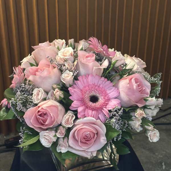 Pink roses and a gerbera daisy arranged in a square vase