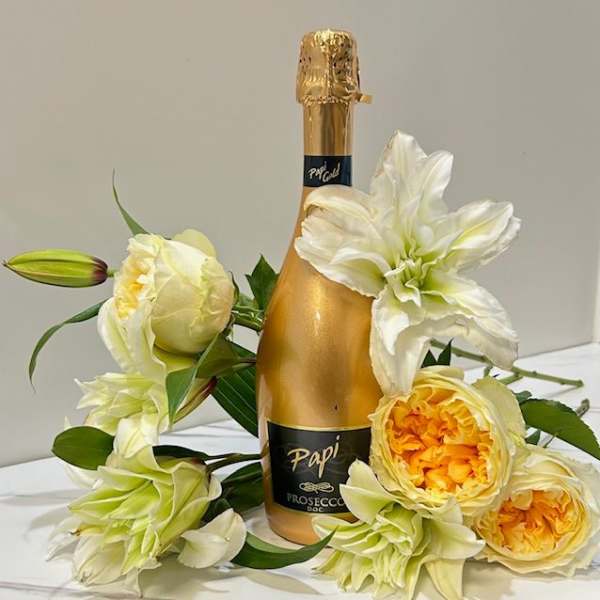 Gold Prosecco bottle surrounded by cream and yellow flowers