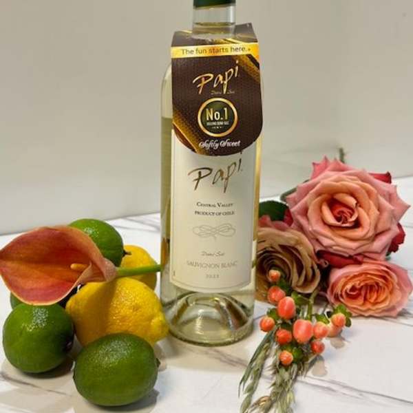 Wine bottle with roses, citrus, and a calla lily on a white surface