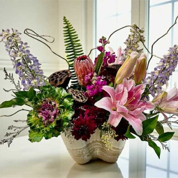 Mixed bouquet with pink lilies and purple flowers in a cream vase