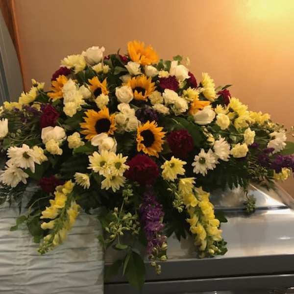Large floral casket spray with sunflowers, white roses, and daisies