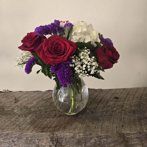 Bouquet of red roses, white hydrangea, and purple filler in a clear glass vase
