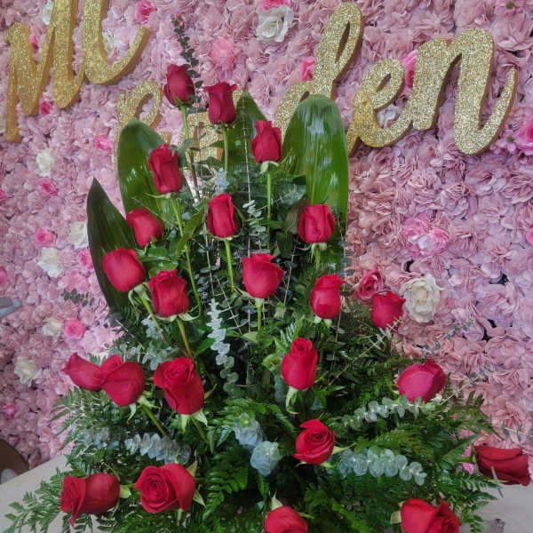 Red rose arrangement against a pink floral wall with gold lettering