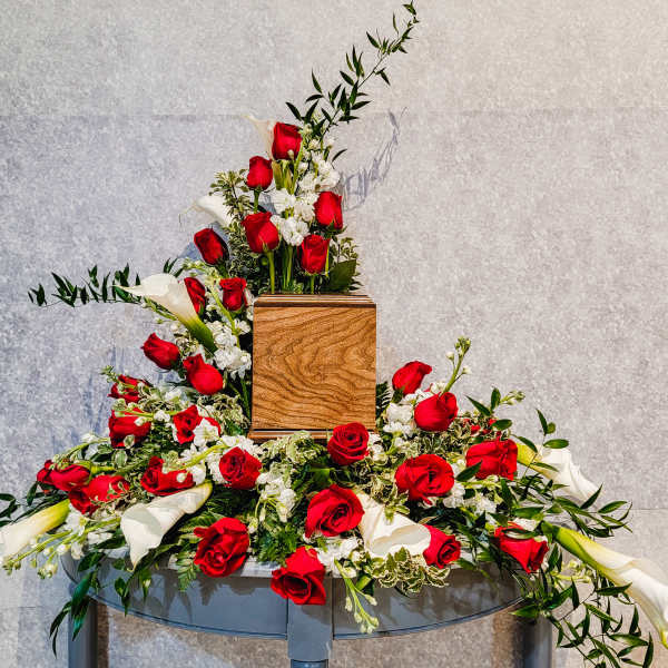 Large floral arrangement with red roses and white calla lilies around a wooden urn