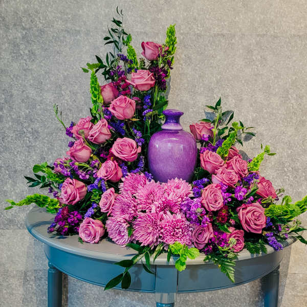 Pink roses and purple flowers arranged around a purple vase on a table