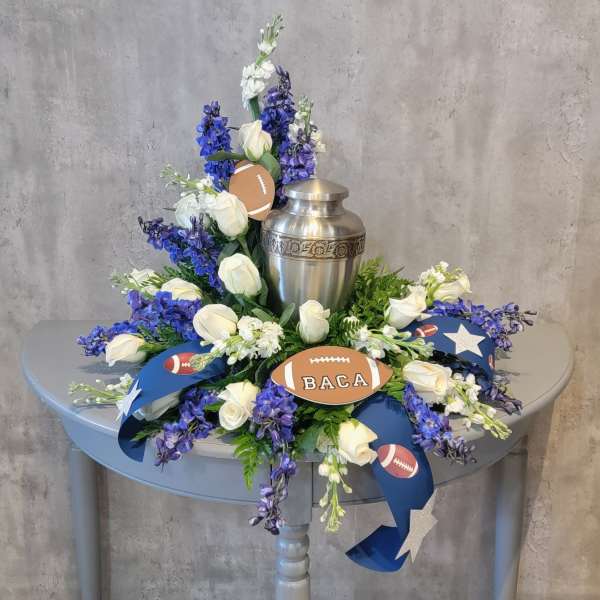White roses and blue-purple flowers arranged around a silver urn with football decorations