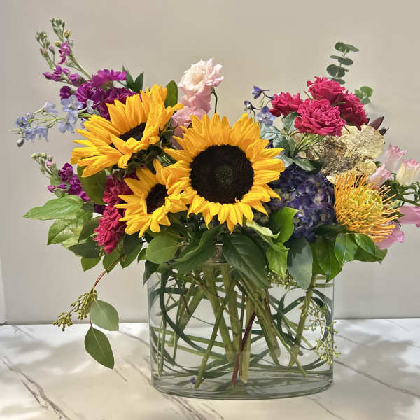 Mixed bouquet with sunflowers, hydrangeas, and pink blooms in a glass vase