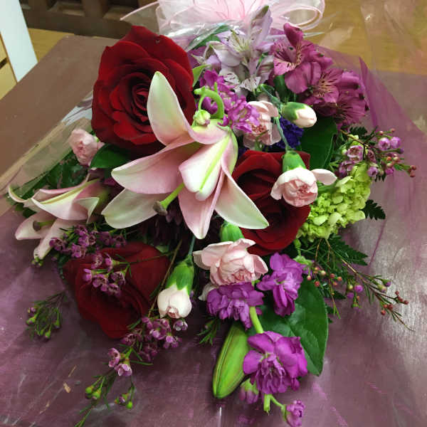 Bouquet of red roses, pink lilies, and purple flowers wrapped in clear cellophane