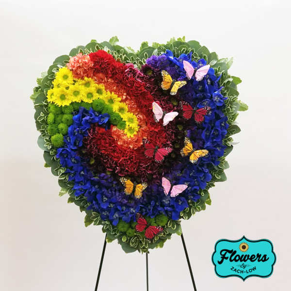 Heart-shaped floral arrangement in rainbow colors with butterfly accents on a stand