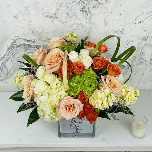 Mixed bouquet of peach, orange, and white roses in a square glass vase
