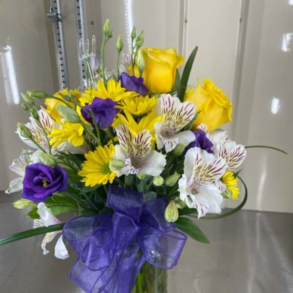 Bouquet of yellow roses, purple lisianthus, and white alstroemeria in a glass vase