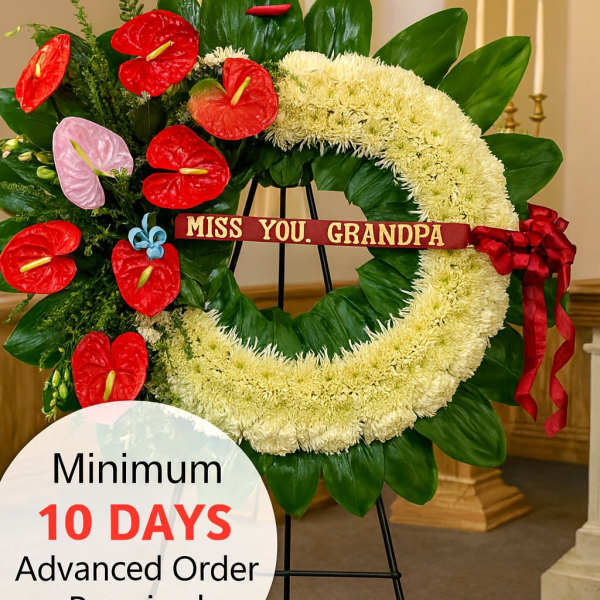 Large white sympathy wreath with red and pink flowers on a stand and a ribbon reading 'Miss you, Grandpa'