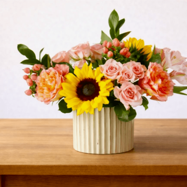 Mixed bouquet with sunflowers, pink roses, and carnations in a ribbed vase