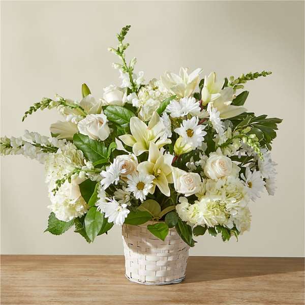 White floral arrangement in a woven basket with daisies and lilies
