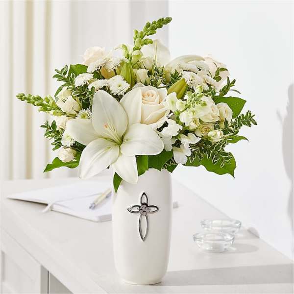 White floral arrangement in a tall vase with a cross emblem
