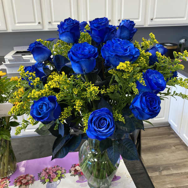 Bouquet of vivid blue roses with yellow filler flowers in a glass vase