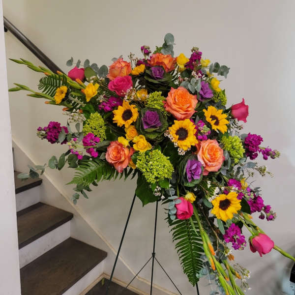 Large standing floral spray with roses, sunflowers, and purple blooms