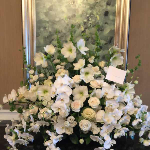 Large white floral arrangement with orchids and roses in a black container