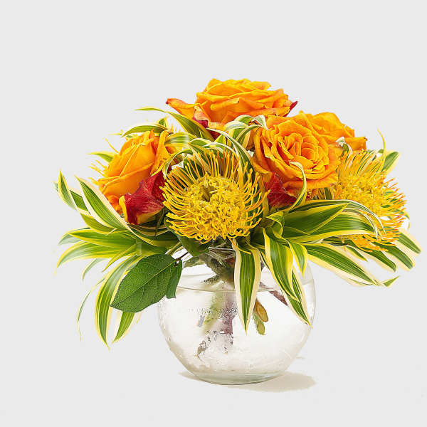 Orange roses and yellow flowers in a clear glass vase