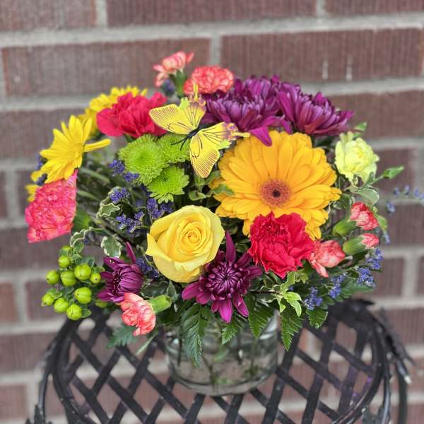 Colorful mixed bouquet in a clear glass vase with a butterfly pick