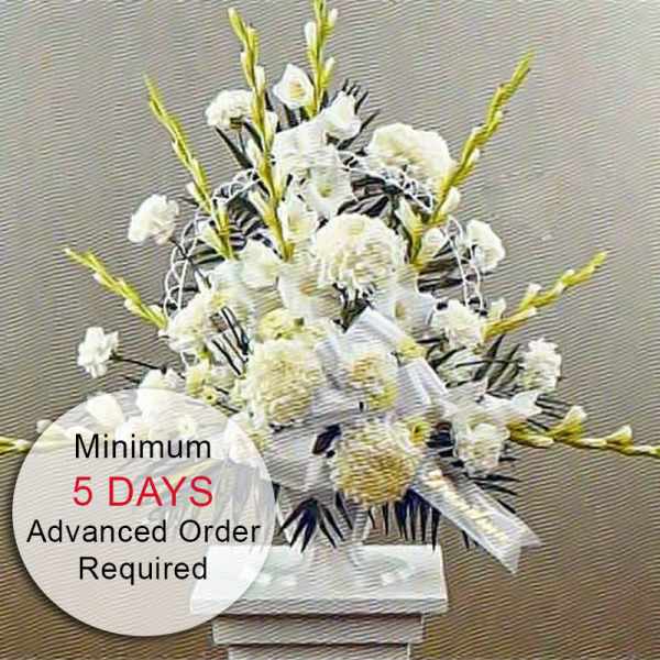 Tall white funeral-style flower arrangement on a pedestal with a white bow.
