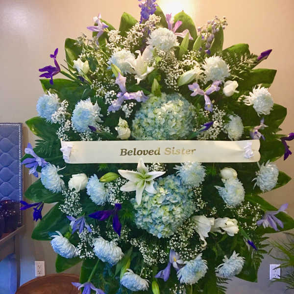 Large sympathy spray with white and lavender flowers and a "Beloved Sister" ribbon