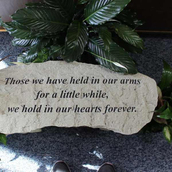 Memorial stone with engraved sympathy message surrounded by green plants