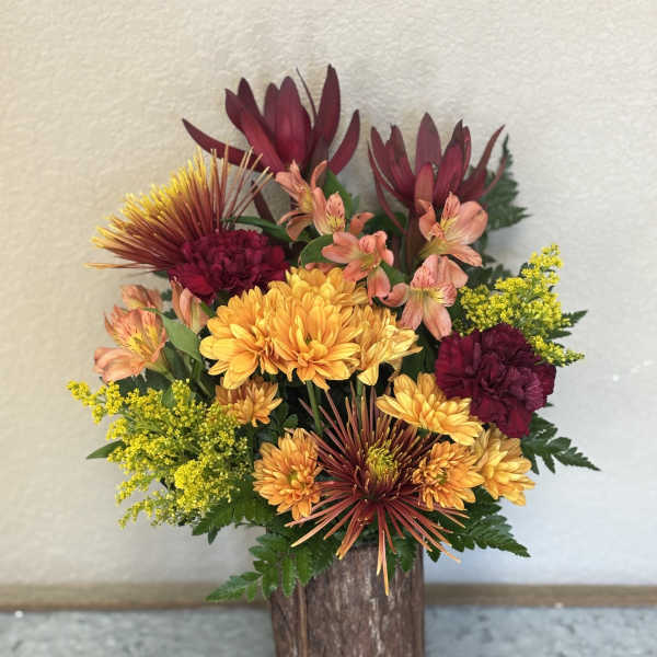Mixed bouquet of orange, burgundy, and yellow flowers in a rustic wooden vase