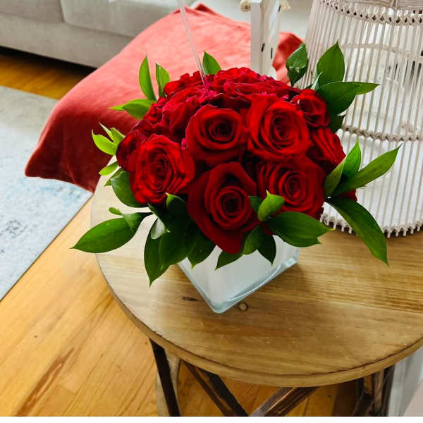Red roses arranged in a square glass vase with green leaves
