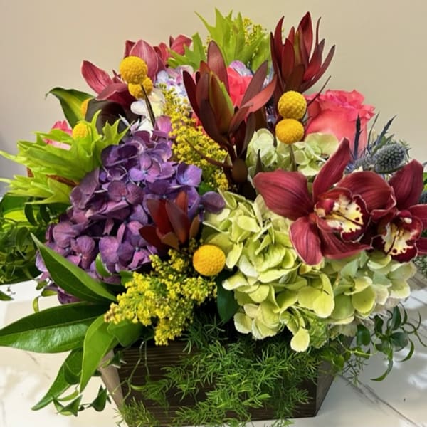 Mixed floral arrangement in a rectangular wooden container with a candle beside it